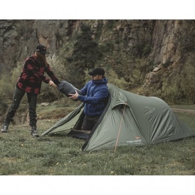 Tunnelzelt Reindal 2 in natürlicher Umgebung, zwei Personen tragen einen Schlafsack durch den offenen Zelteingang.